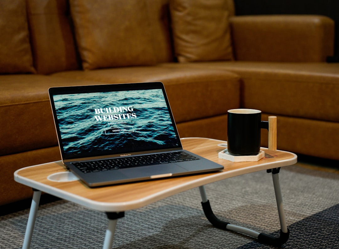 Build websites for your portfolio, resume, internal communications, etc. A laptop, MacBook, on top of a portable table with coffee tea mug on the side.